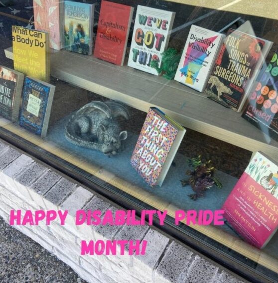 a window display features fiction and non-fiction books with positive disabled representation surrounded by dragon statutes. "Happy Disability Pride Month!" is written along the bottom of the picture in pink font.